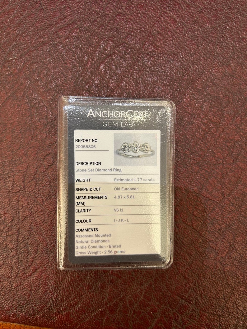 Puede incluir: Un primer plano de un anillo de diamantes con un certificado de Anchorcert Gem Lab. El anillo es un anillo de diamantes engastados con un peso estimado de 1,77 quilates. El diamante es un corte antiguo europeo con medidas de 4,87 x 5,81 mm. La claridad del diamante es VS 11 y el color es I-JK-L. El certificado tambi&eacute;n indica que los diamantes son naturales y que la condici&oacute;n de la cintura es bruta. El peso bruto del anillo es de 2,56 gramos.