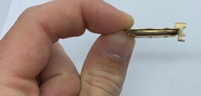 May include: A gold-colored metal key with a unique design. The key has a curved body and a small, intricate handle.