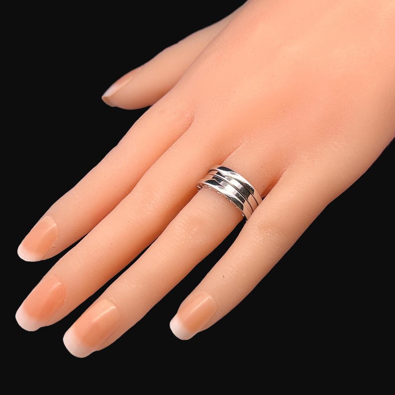 May include: A silver ring with three bands, each with a slightly different texture. The ring is worn on a model's finger.