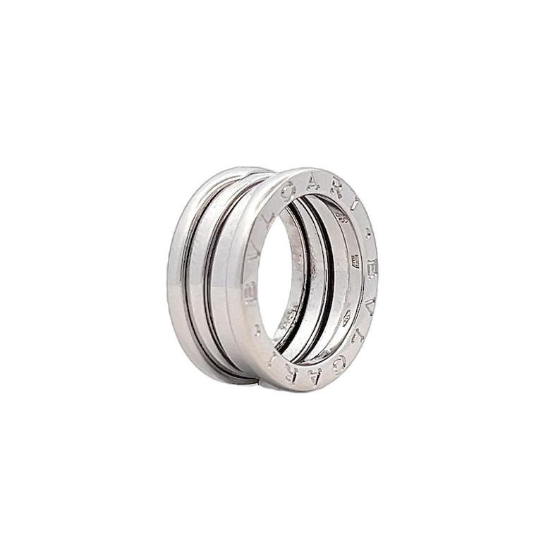 May include: A silver ring with a triple band design. The ring is engraved with the letters "BVLGARI" around the outer band.