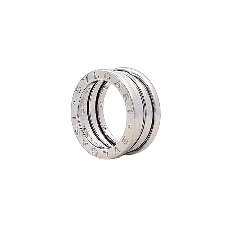 May include: A silver ring with the word "BVLGARI" engraved around the band. The ring is made up of three bands that are stacked on top of each other.