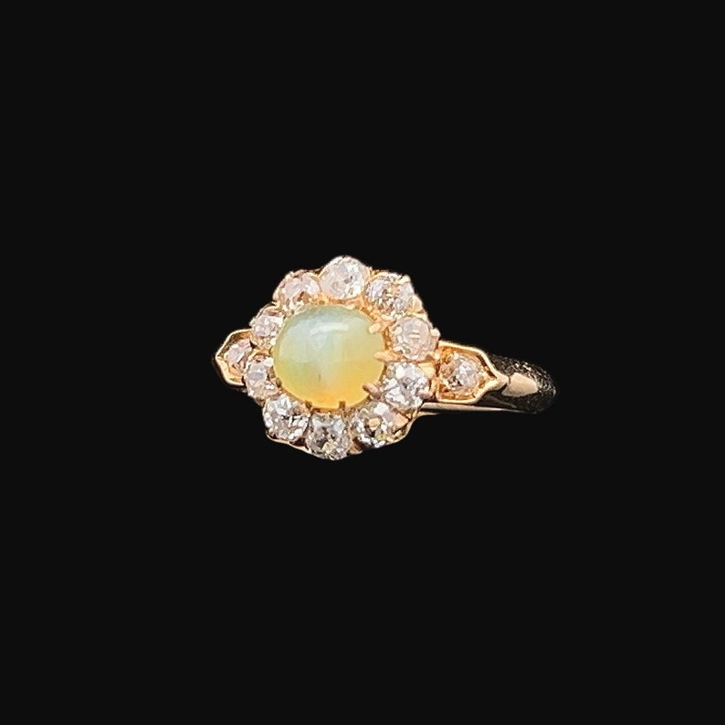 May include: A gold ring with a round, pale green opal gemstone surrounded by a halo of smaller diamonds.