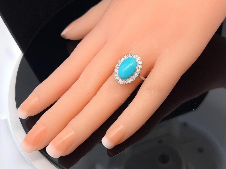 May include: A turquoise oval gemstone ring set in a white gold band with a halo of small diamonds.