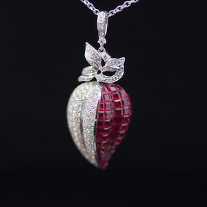 May include: A silver pendant necklace with a unique design. The pendant features a half-red, half-silver jewel-like shape, with a leaf-like design at the top. The red side has a textured, blocky appearance, while the silver side is encrusted with small, sparkling stones.