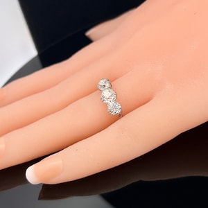 Puede incluir: Un anillo de plata con tres diamantes redondos engastados en fila. Los diamantes est&aacute;n rodeados de diamantes m&aacute;s peque&ntilde;os.
