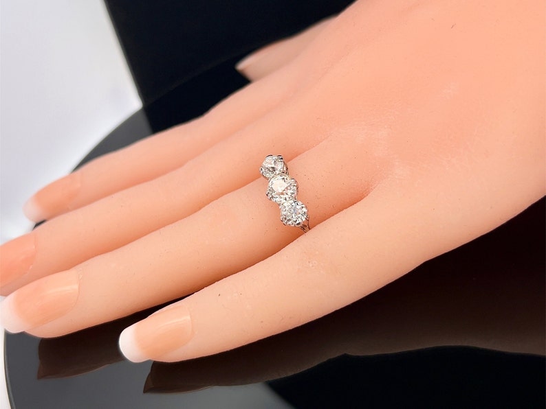 Puede incluir: Un anillo de plata con tres diamantes redondos engastados en fila. Los diamantes est&aacute;n rodeados de diamantes m&aacute;s peque&ntilde;os.