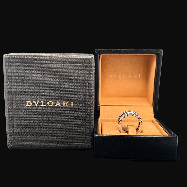May include: A silver ring with the word "BVLGARI" engraved on it, inside a black and brown box with the same brand name.