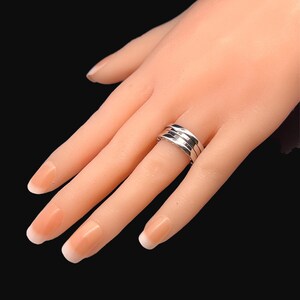 May include: A silver ring with three bands, each with a slightly different texture. The ring is worn on a model's finger.