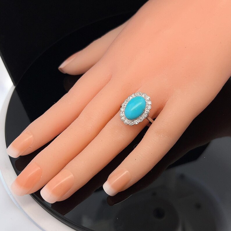 May include: A turquoise oval gemstone ring with a halo of small diamonds set in white gold.