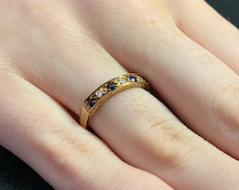 May include: A gold band ring with a row of alternating blue and white gemstones.