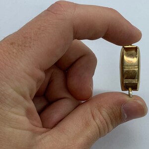 May include: A gold-colored metal watch band with a clasp. The band is held in a hand.