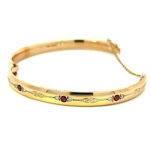 May include: A gold bangle bracelet with a delicate design and red and white gemstones.