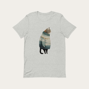 May include: A grey t-shirt featuring a cartoon illustration of a cat wearing a blue and white striped jumper.