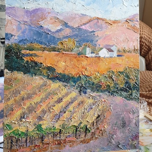 May include: A painting depicting a landscape with a white farmhouse in the distance. The foreground features a vineyard with rows of grapevines and a dirt road leading up to the farmhouse. The sky is blue with white clouds and the mountains are a mix of purple, brown, and green.