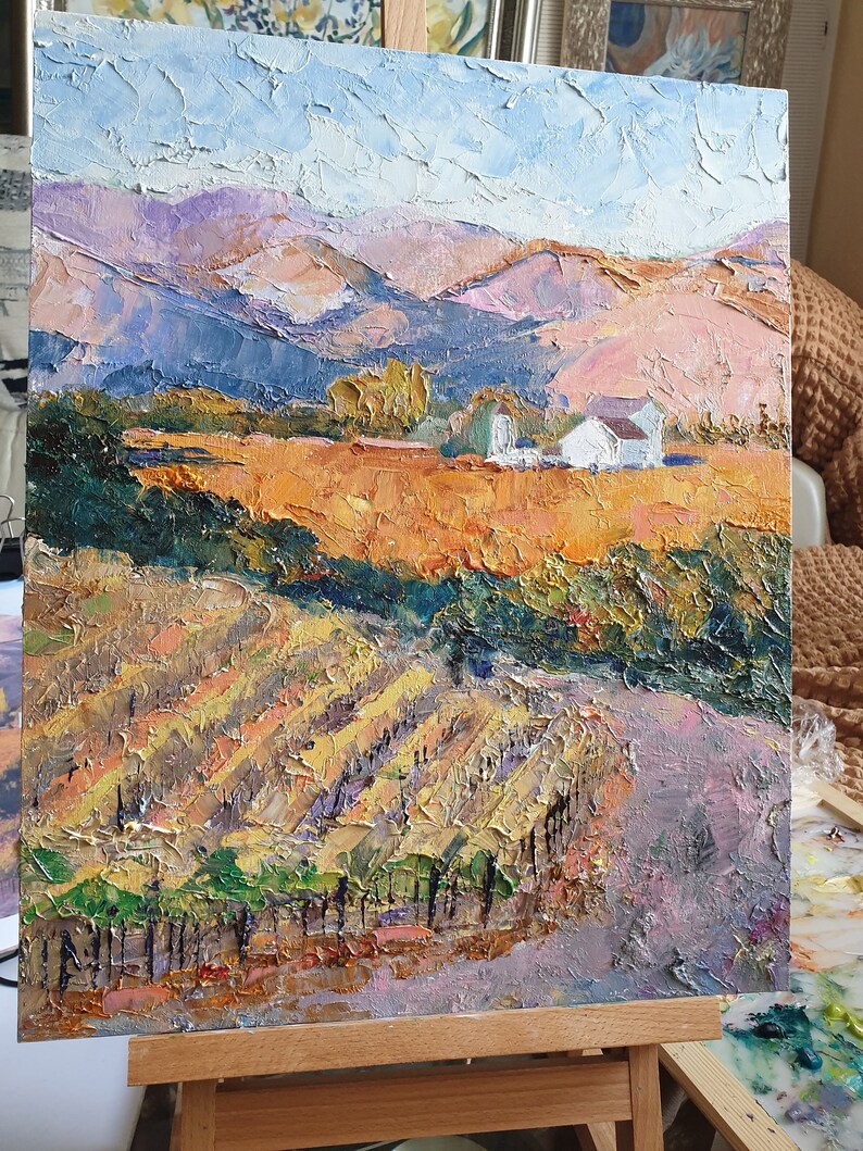 May include: A painting depicting a landscape with a white farmhouse in the distance. The foreground features a vineyard with rows of grapevines and a dirt road leading up to the farmhouse. The sky is blue with white clouds and the mountains are a mix of purple, brown, and green.