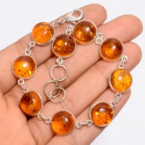 Könnte beinhalten: Ein silbernes Armband mit runden Bernstein-Edelsteinen. Das Armband hat einen Karabinerverschluss und ist aus Sterlingsilber gefertigt.