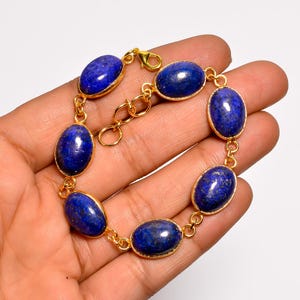 May include: A gold-toned bracelet featuring oval-shaped, deep blue lapis lazuli stones. The stones are set in gold bezels and linked together with delicate gold chain. The bracelet is designed to be worn around the wrist.