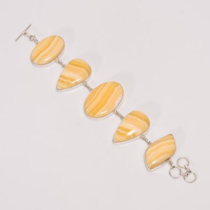 May include: A silver bracelet featuring five oval and teardrop-shaped, polished yellow gemstones with brown striations. The bracelet has a toggle clasp and a series of small silver links connecting the stones. The gemstones are set in silver bezels.