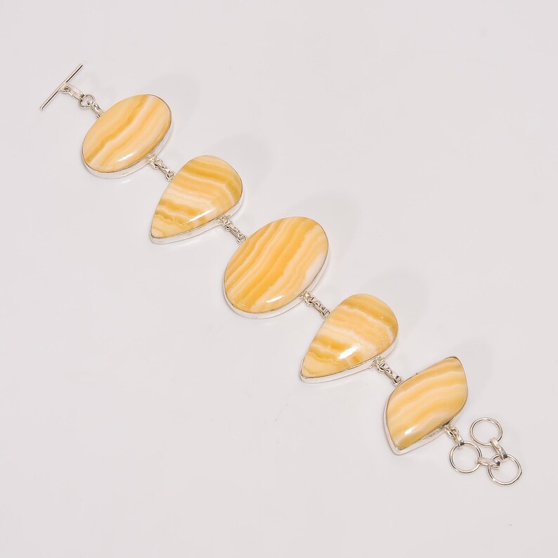 May include: A silver bracelet featuring five oval and teardrop-shaped, polished yellow gemstones with brown striations. The bracelet has a toggle clasp and a series of small silver links connecting the stones. The gemstones are set in silver bezels.