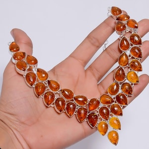 Könnte beinhalten: Eine silberne Halskette mit bernsteinfarbenen tropfenförmigen Steinen. Die Halskette ist aus Sterlingsilber gefertigt und hat eine zarte Kette mit einem Anhänger, der mit mehreren Bernstein-Steinen verziert ist.