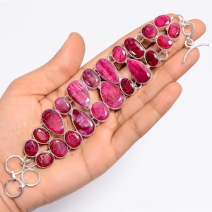 May include: A silver bracelet featuring multiple oval and teardrop-shaped ruby gemstones. The rubies are a deep pink color and are set in a silver metal frame. The bracelet has a toggle clasp.