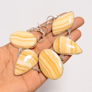May include: A silver bracelet featuring six polished, oval and teardrop-shaped stones with a creamy yellow and white striped pattern. The stones are connected by silver links and a toggle clasp.