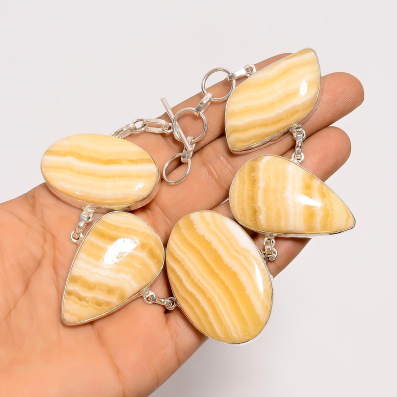 May include: A silver bracelet featuring six polished, oval and teardrop-shaped stones with a creamy yellow and white striped pattern. The stones are connected by silver links and a toggle clasp.