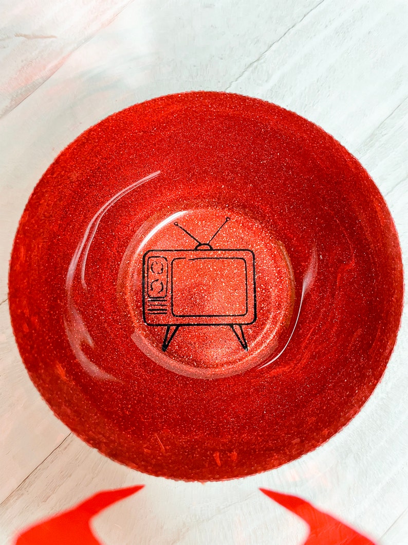 Op de afbeelding: Een rode glitterkom met een zwarte omtrek van een vintage televisie in het midden.