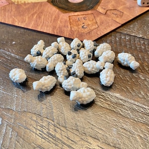 Peut inclure: Gros plan sur un groupe de pions de jeu en forme de moutons blancs avec des yeux noirs. Les moutons sont sur une surface en bois.