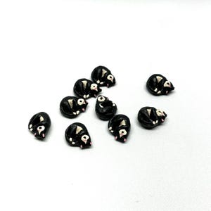 May include: A collection of small, black and white skunk figurines. Each skunk is curled up in a sleeping position, with a pink nose and white stripe. The figurines are scattered on a white surface.