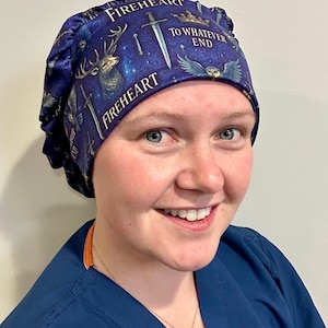 May include: A navy blue scrub cap with a celestial design featuring a stag, swords, and the words "FIREHEART" and "TO WHATEVER END." The cap is made of a soft fabric and is worn by a person.