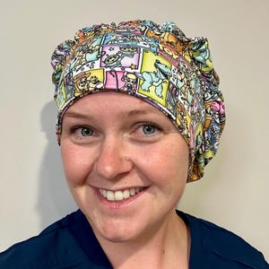 May include: A scrub cap featuring a colorful comic book style print with various cartoon characters from Toy Story, including Rex, Bo Peep, and the aliens, set against a grid of yellow, pink, and white squares with stars and text accents.