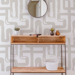 May include: A wooden console table with a metal frame and two shelves. The table is decorated with a round mirror, two potted plants, and a white wicker basket. The wall behind the table is covered in a beige and white geometric wallpaper.