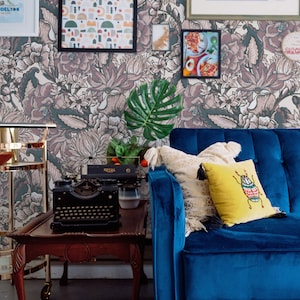 May include: Interior shot of a living room with a dark wood table holding a vintage typewriter. A blue velvet sofa is set against floral wallpaper and framed art, including an abstract painting and a geometric print.