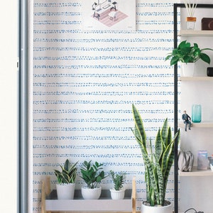 May include: A white shelf unit with three shelves, each holding various items, including plants, a small figurine, and a diffuser. The wall behind the shelf is decorated with a blue and white patterned wallpaper.
