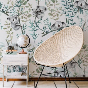 May include: A white wicker chair with black metal legs sits in front of a wall with a watercolour pattern of koalas and eucalyptus leaves.