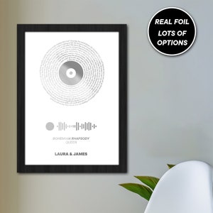 May include: A black framed print with a silver record design featuring the lyrics to the song "Bohemian Rhapsody" by Queen. The print also includes a barcode and the names "Laura & James".