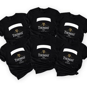 May include: Black t-shirts with white and gold text. Each shirt has a white banner and the name "Thomas" with "Stag" below. The text below the name varies: "The Best Man", "The Groomsman", "The Usher", "Father of the Bride", and "The Groom".