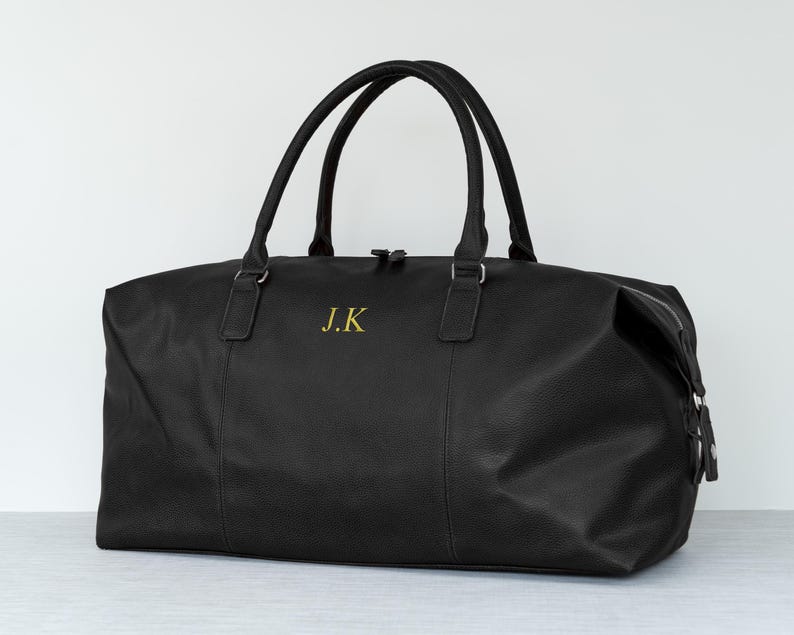 May include: Black leather travel duffel bag with a zipper closure and two top handles. The bag has the initials "J.K." embroidered on the front in gold thread.