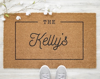 May include: A brown coir doormat with the text "THE Kelly's" in a black rectangular frame.