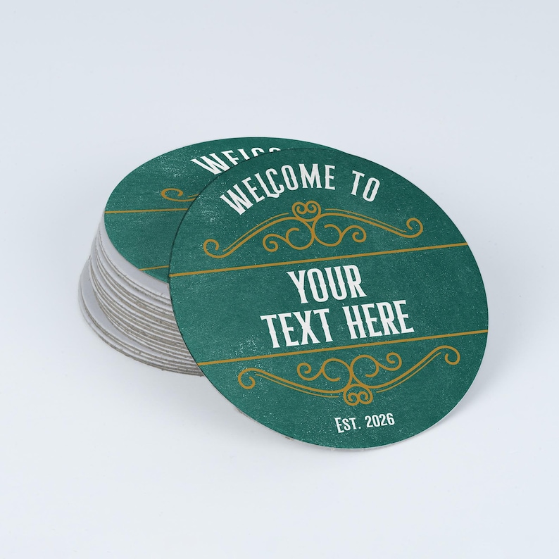 Peut inclure: Une pile de sous-verres circulaires sur fond bleu sarcelle fonc&eacute;. Le sous-verre sup&eacute;rieur pr&eacute;sente le texte blanc "WELCOME TO", "YOUR TEXT HERE" et "EST. 2026". Des fioritures d&eacute;coratives dor&eacute;es et des lignes horizontales encadrent le texte.