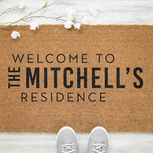 May include: A brown coir doormat with the text "Welcome to The Mitchell's Residence" in black lettering.