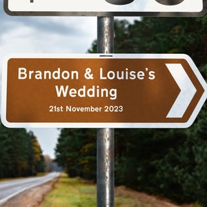 May include: A brown directional sign with a white arrow pointing to the right. The sign reads "Brandon & Louise's Wedding 21st November 2023".