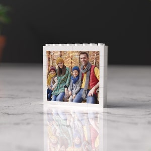 May include: A white photo block with a picture of a family of four in a forest setting. The family is wearing fall-themed clothing and smiling at the camera.