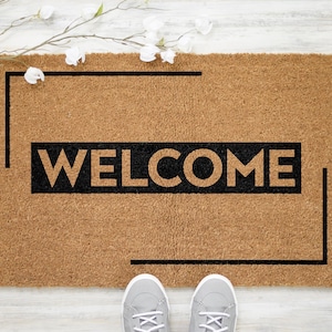 May include: A brown coir doormat with a black border and the word "WELCOME" in black lettering.