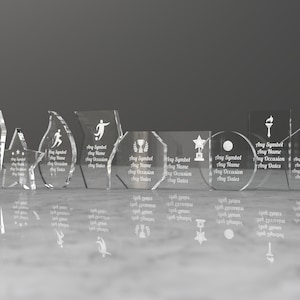 K&ouml;nnte beinhalten: Ein Satz von acht klaren Glas-Preistafeln mit verschiedenen Formen und Designs. Jede Tafel hat Platz f&uuml;r ein Symbol, einen Namen, einen Anlass und Daten. Die Tafeln sind in einer Reihe auf einer wei&szlig;en Oberfl&auml;che angeordnet.