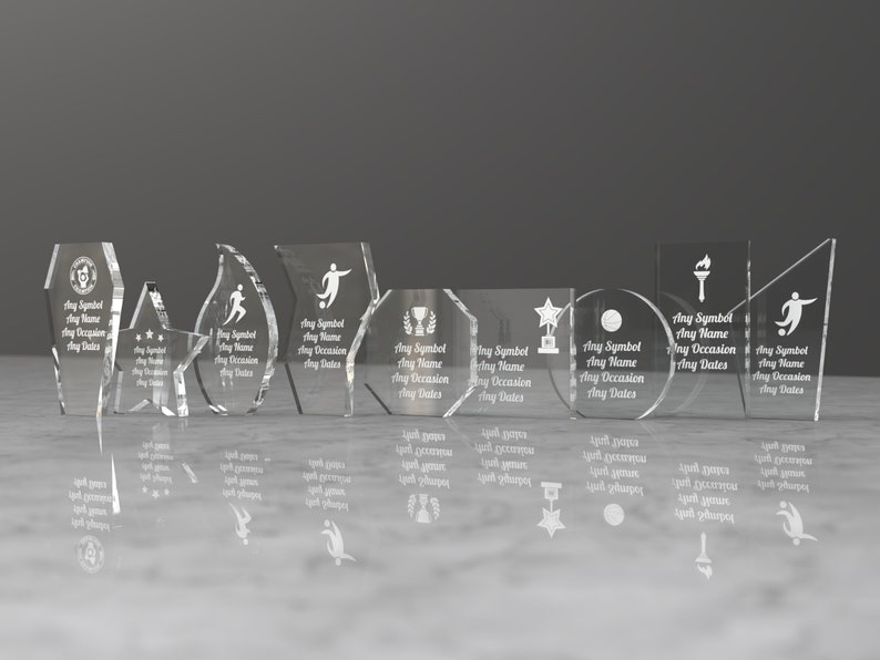 K&ouml;nnte beinhalten: Ein Satz von acht klaren Glas-Preistafeln mit verschiedenen Formen und Designs. Jede Tafel hat Platz f&uuml;r ein Symbol, einen Namen, einen Anlass und Daten. Die Tafeln sind in einer Reihe auf einer wei&szlig;en Oberfl&auml;che angeordnet.