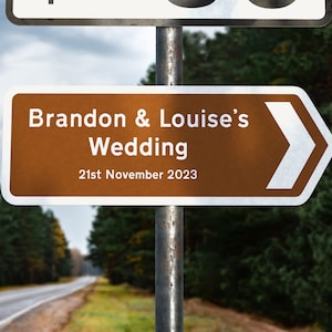 May include: A brown and white directional sign with an arrow pointing to the right. The sign reads "Brandon & Louise's Wedding 21st November 2023".