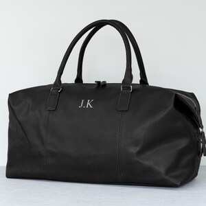 May include: Black leather travel duffel bag with a zipper closure and a silver monogram "J.K."