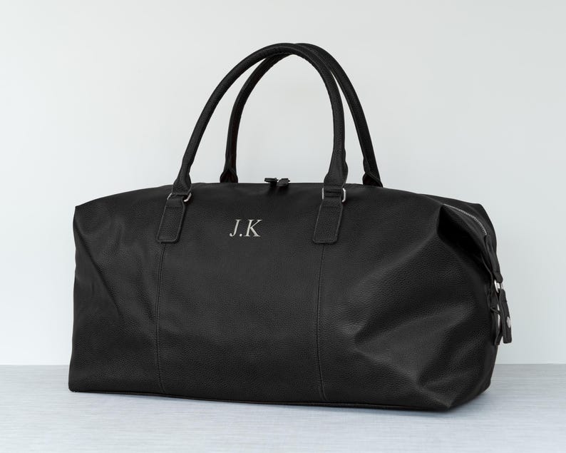 May include: Black leather travel duffel bag with a zipper closure and a silver monogram "J.K."